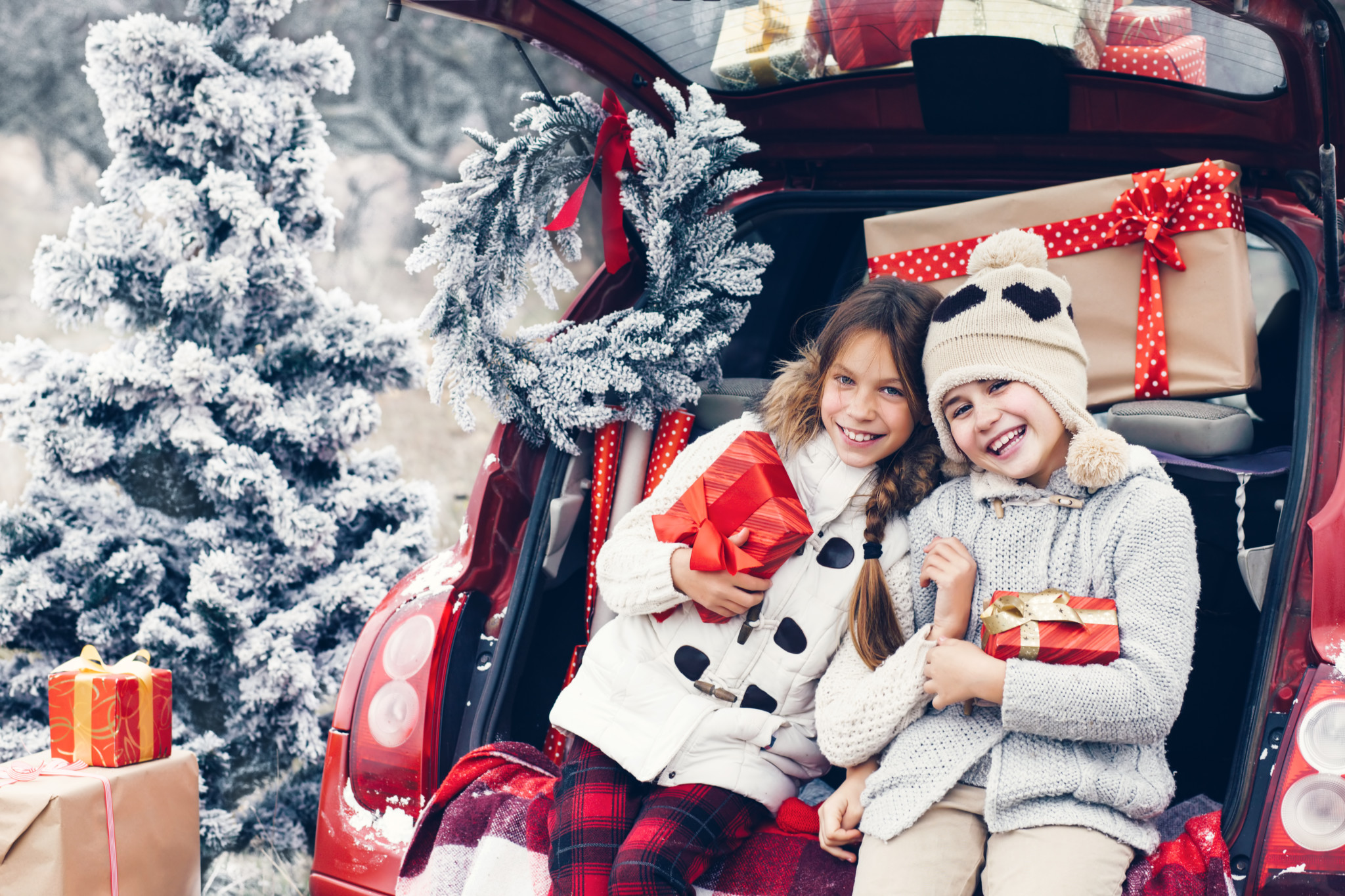 Holiday preparations. Pre teen children enjoy many Christmas presents in car trunk. Cold winter, snow weather.